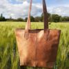 sac cabas en cuir couleur claire tenu à bout de bras dans un champ