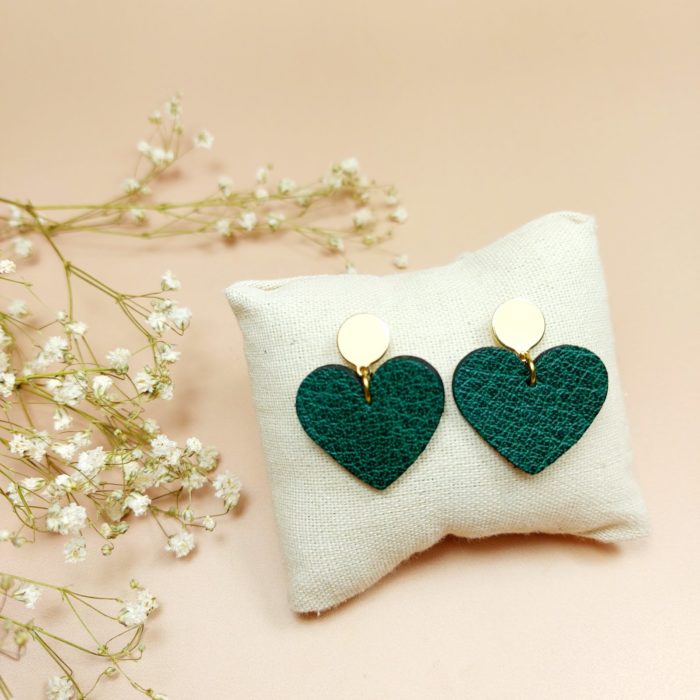 Boucles d'oreilles en cuir vert en forme de coeur présentées sur un coussin