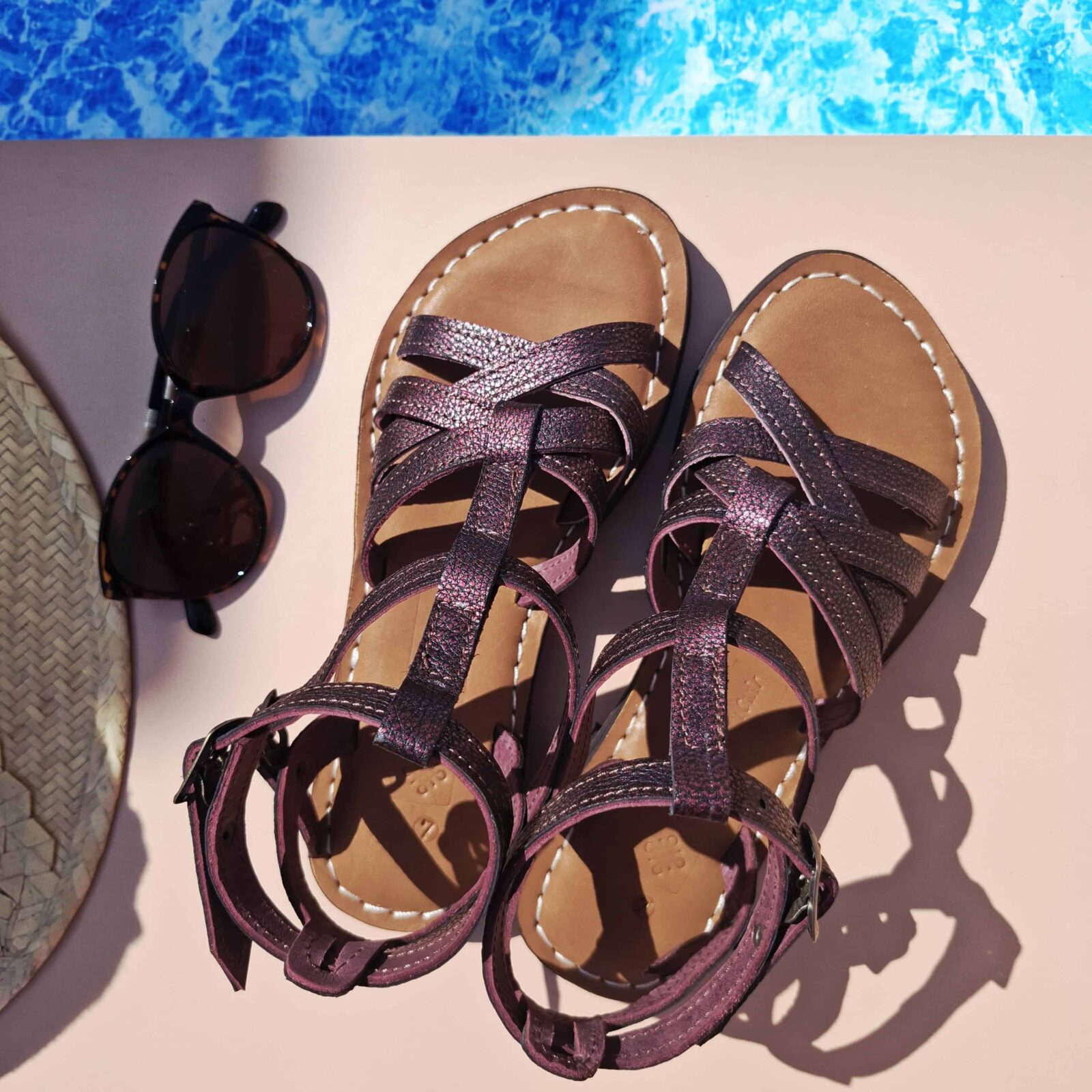 Sandales Helena en cuir bordeaux posées au bord de la piscine avec lunettes de soleil