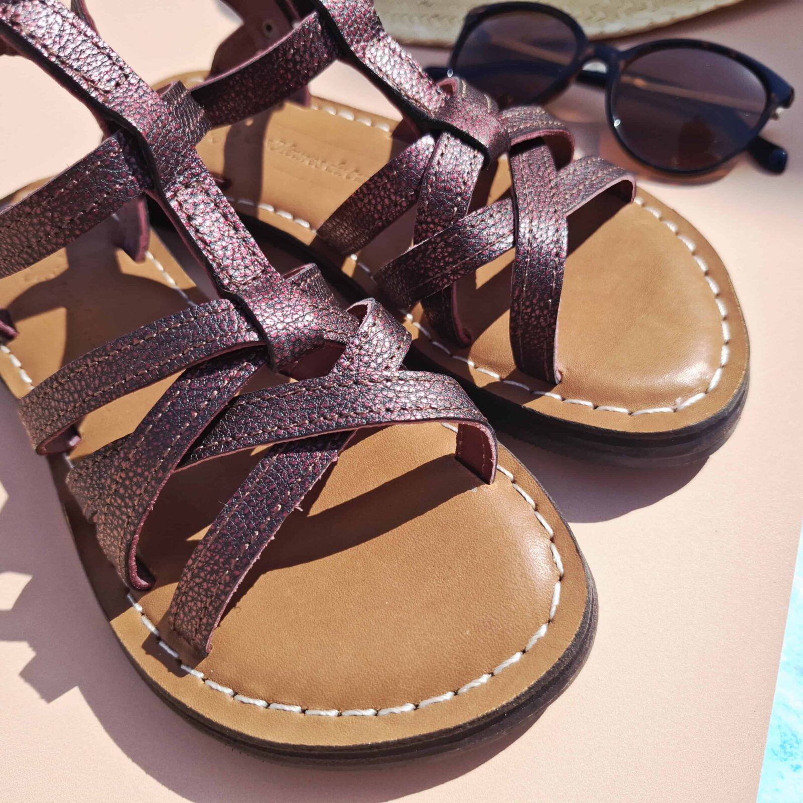 Paire de sandales cuir bordeaux Helena posées de face avec chapeau de paille et lunettes de soleil