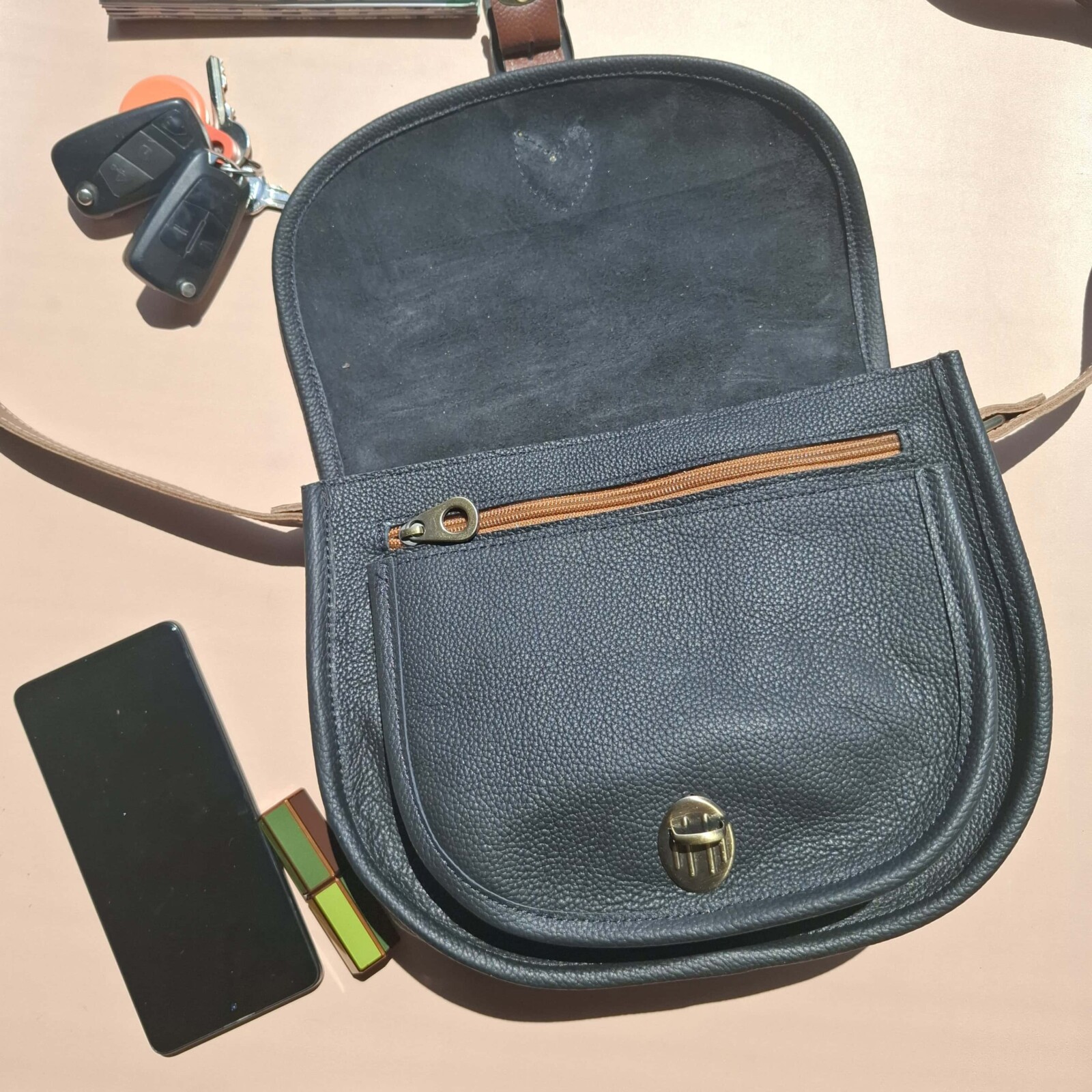 Intérieur du sac besace cuir noir grainé Simone ouvert : rabat, poche zip et fermoir twist vus de dessus