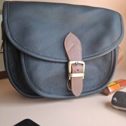 Sac besace cuir noir grainé Simone vu de trois quarts : boucle laiton et patte cuir naturel