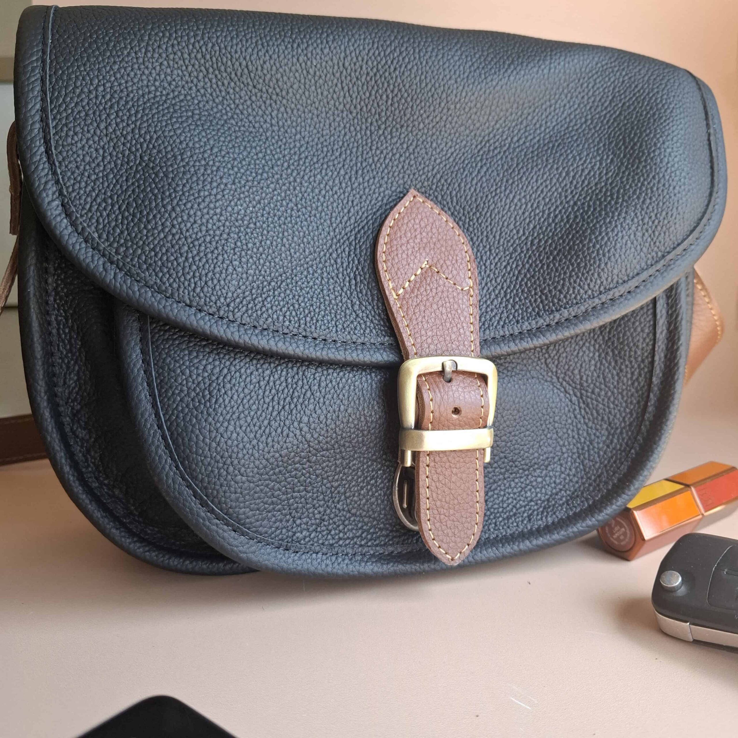 Sac besace cuir noir grainé Simone vu de trois quarts : boucle laiton et patte cuir naturel
